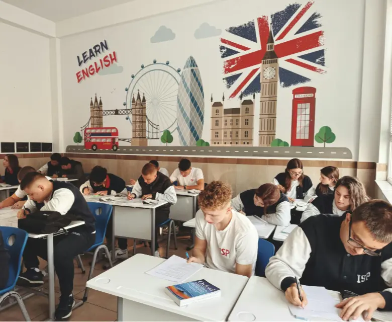 Estudiantes concentrados en clase con un mural de monumentos británicos de fondo durante un programa de año escolar.